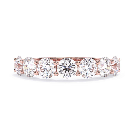 A picture of a seven stone diamond wedding ring with round diamonds that are U prong set in rose gold on a white background with the ring facing forward, lying down.