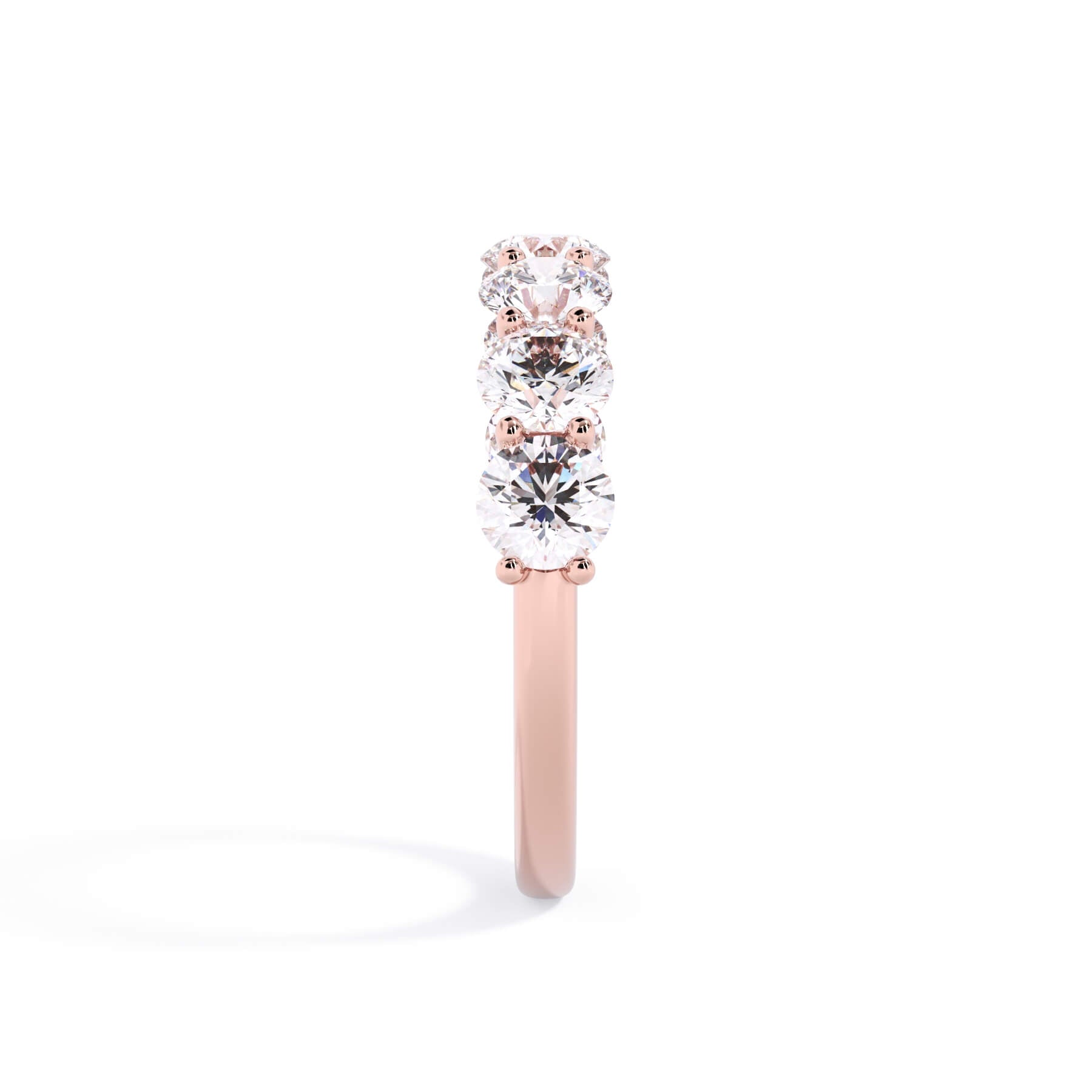 A picture of a seven stone diamond wedding ring with round diamonds that are U prong set in rose gold on a white background with a side profile view.