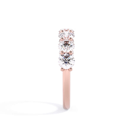 A picture of a seven stone diamond wedding ring with round diamonds that are U prong set in rose gold on a white background with a side profile view.