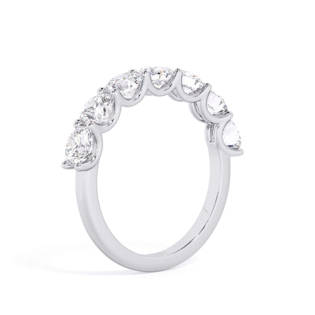 A picture of a seven stone diamond wedding ring with round diamonds that are U prong set in white gold or platinum on a white background with a slightly angled, through the finger view.