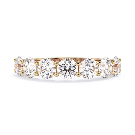 A picture of a seven stone diamond wedding ring with round diamonds that are U prong set in yellow gold on a white background with the ring facing forward, lying down.