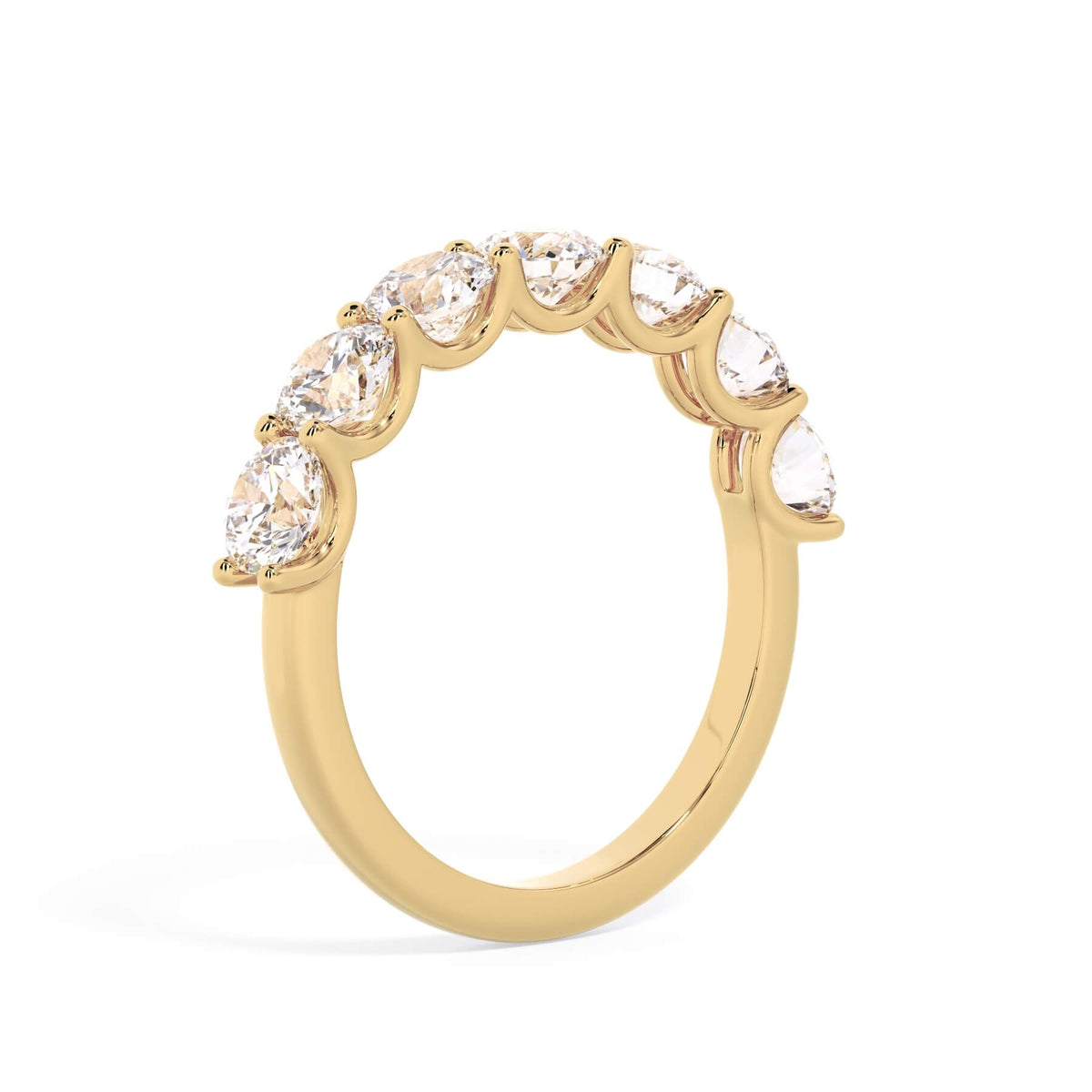 A picture of a seven stone diamond wedding ring with round diamonds that are U prong set in yellow gold on a white background with a slightly angled, through the finger view.