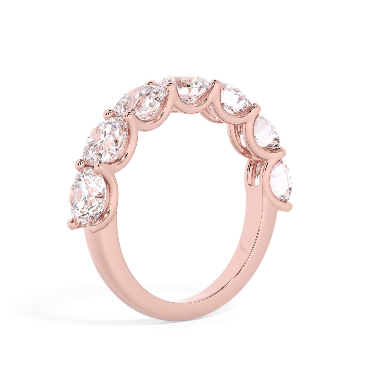 A picture of a seven stone diamond wedding ring with round diamonds that are U prong set in rose gold on a white background with a slightly angled, through the finger view.