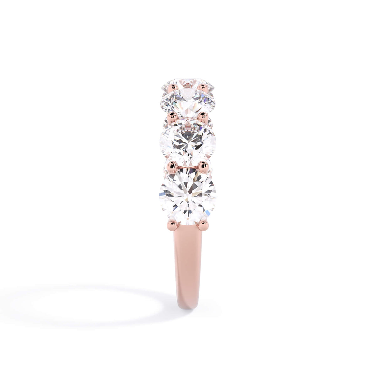 A picture of a seven stone diamond wedding ring with round diamonds that are U prong set in rose gold on a white background with a side profile view.