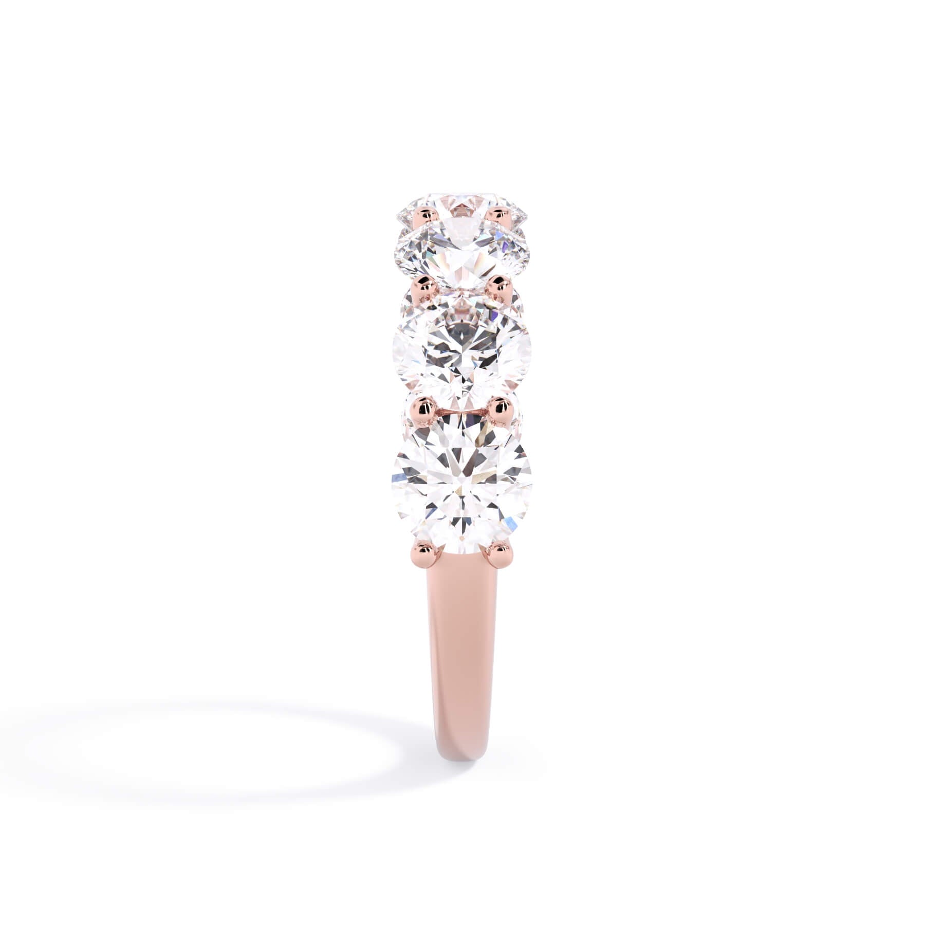 A picture of a seven stone diamond wedding ring with round diamonds that are U prong set in rose gold on a white background with a side profile view.