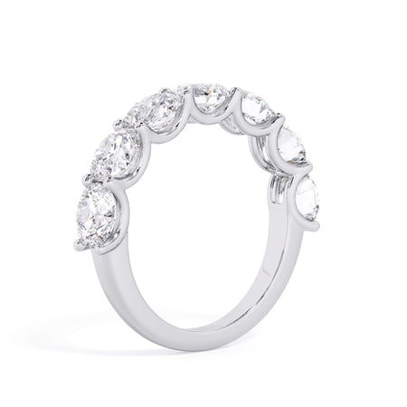 A picture of a seven stone diamond wedding ring with round diamonds that are U prong set in white gold or platinum on a white background with a slightly angled, through the finger view.