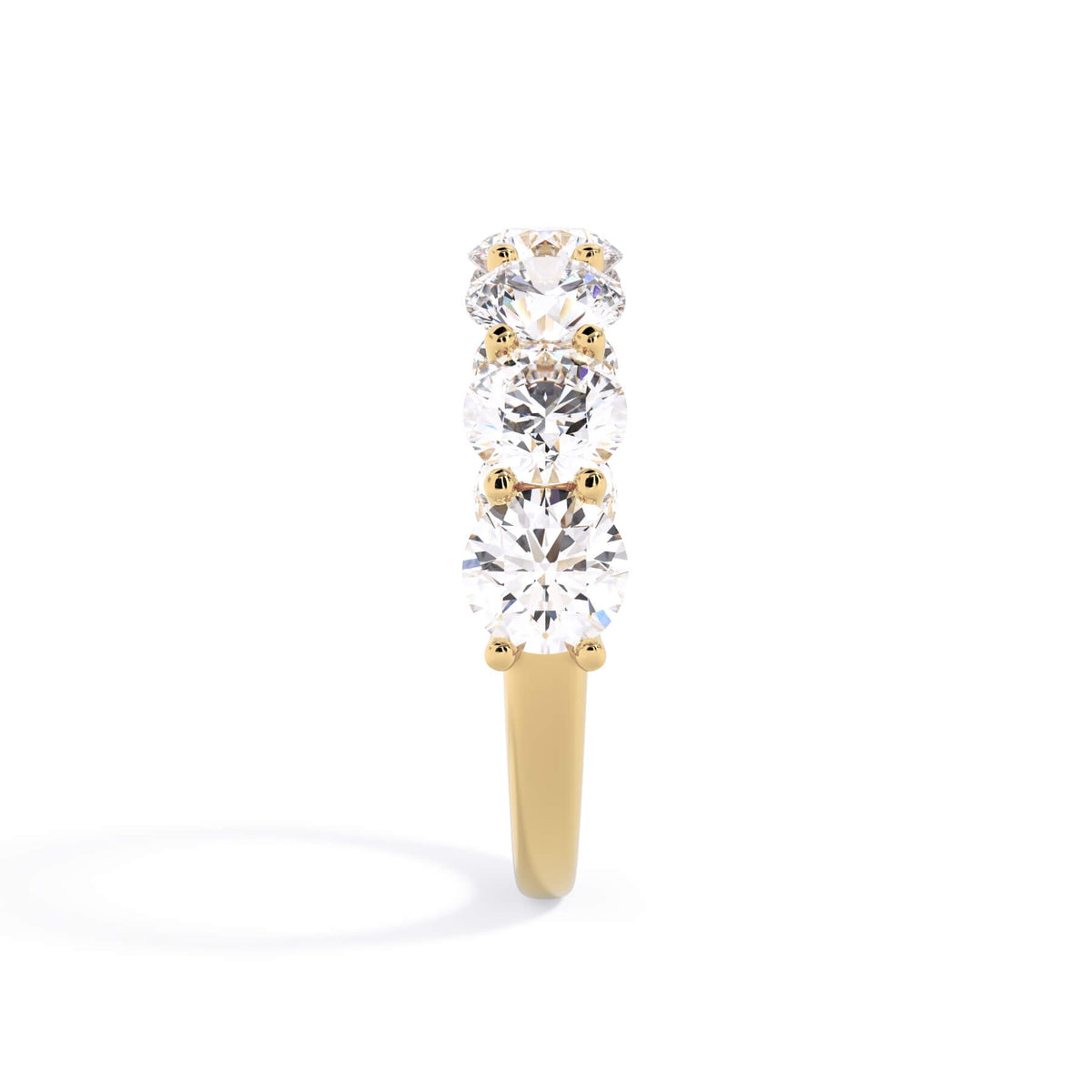 A picture of a seven stone diamond wedding ring with round diamonds that are U prong set in yellow gold on a white background with a side profile view.