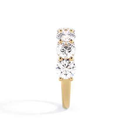 A picture of a seven stone diamond wedding ring with round diamonds that are U prong set in yellow gold on a white background with a side profile view.