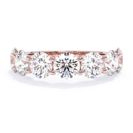 A picture of a seven stone diamond wedding ring with round diamonds that are U prong set in rose gold on a white background with the ring facing forward, lying down.
