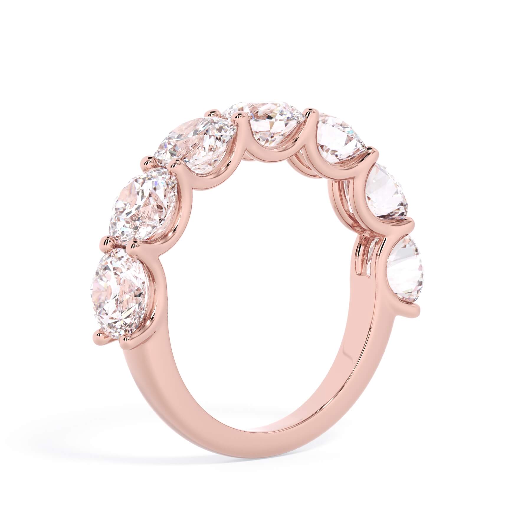 A picture of a seven stone diamond wedding ring with round diamonds that are U prong set in rose gold on a white background with a slightly angled, through the finger view.