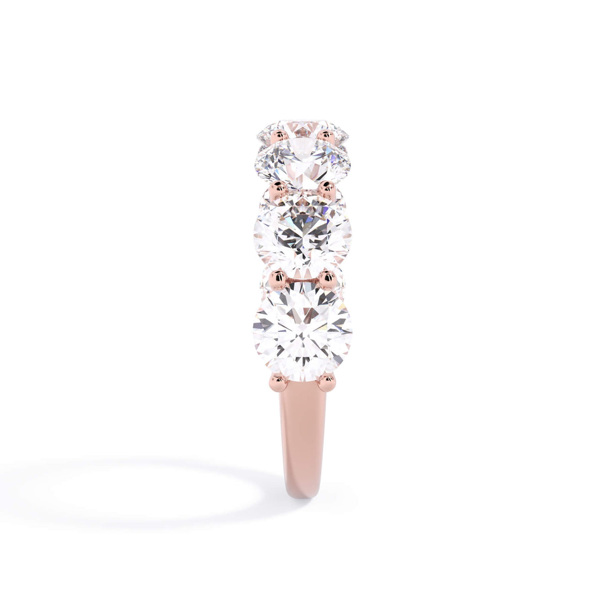 A picture of a seven stone diamond wedding ring with round diamonds that are U prong set in rose gold on a white background with a side profile view.