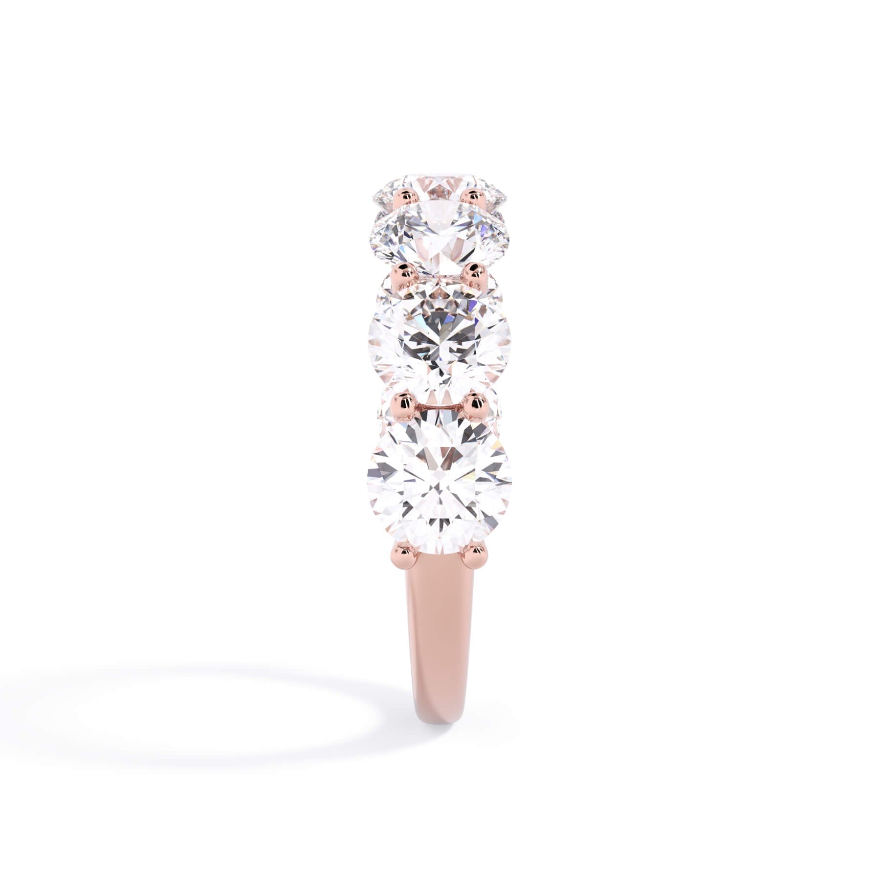 A picture of a seven stone diamond wedding ring with round diamonds that are U prong set in rose gold on a white background with a side profile view.