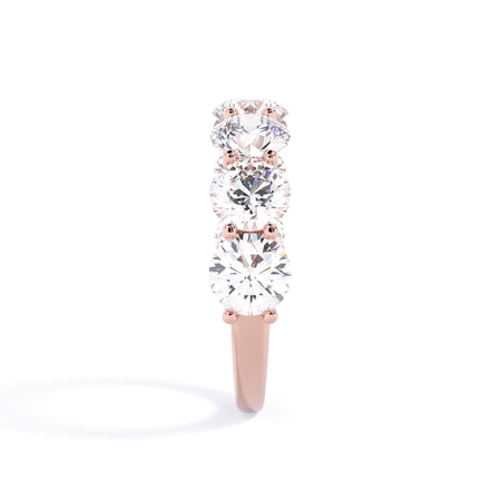 A picture of a seven stone diamond wedding ring with round diamonds that are U prong set in rose gold on a white background with a side profile view.
