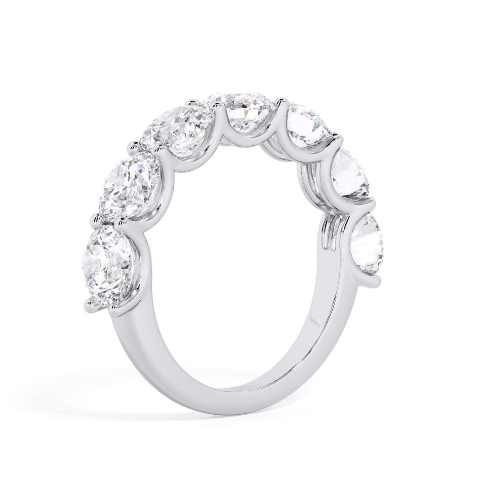 A picture of a seven stone diamond wedding ring with round diamonds that are U prong set in white gold or platinum on a white background with a slightly angled, through the finger view.