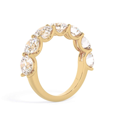 A picture of a seven stone diamond wedding ring with round diamonds that are U prong set in yellow gold on a white background with a slightly angled, through the finger view.