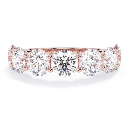 A picture of a seven stone diamond wedding ring with round diamonds that are U prong set in rose gold on a white background with the ring facing forward, lying down.