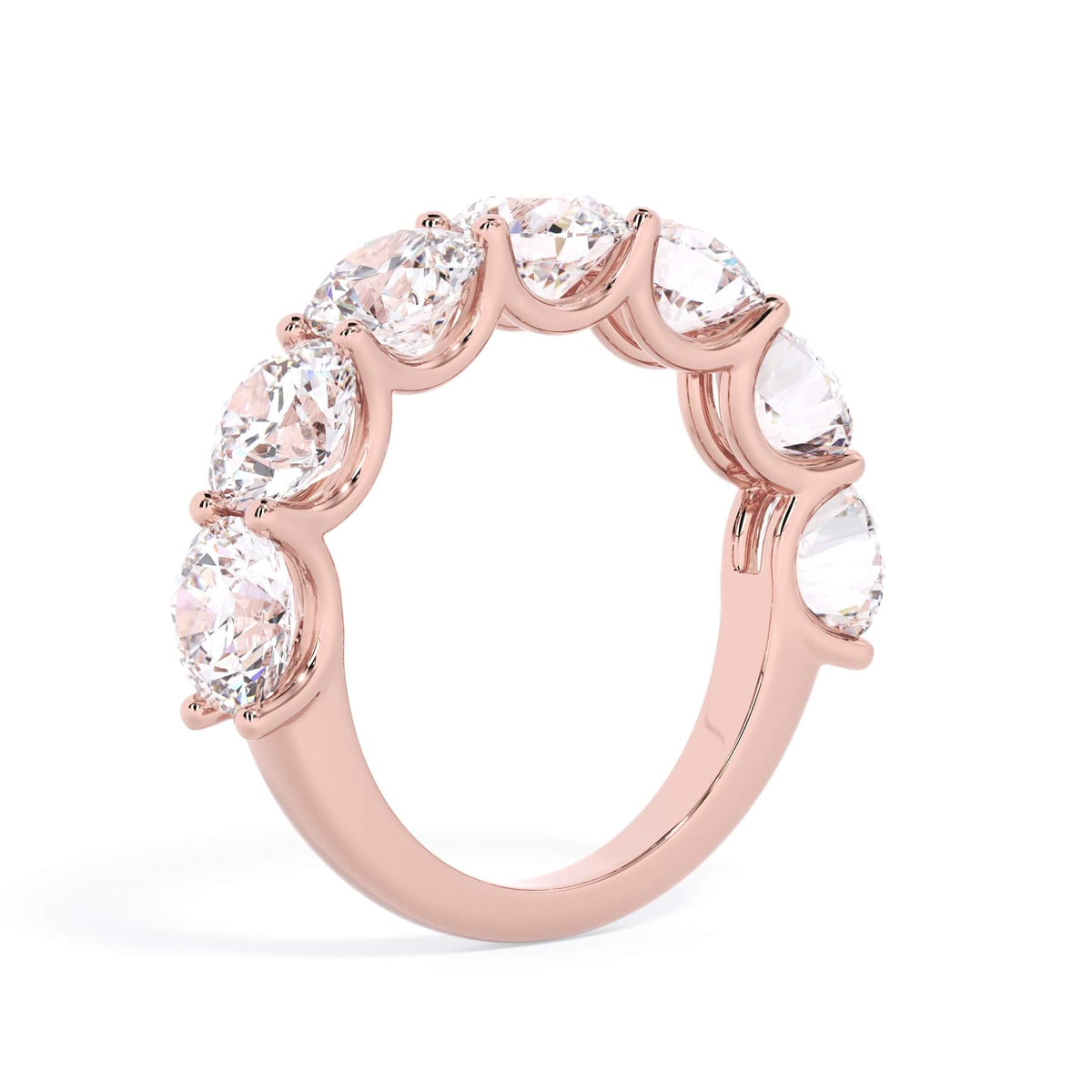 A picture of a seven stone diamond wedding ring with round diamonds that are U prong set in rose gold on a white background with a slightly angled, through the finger view.