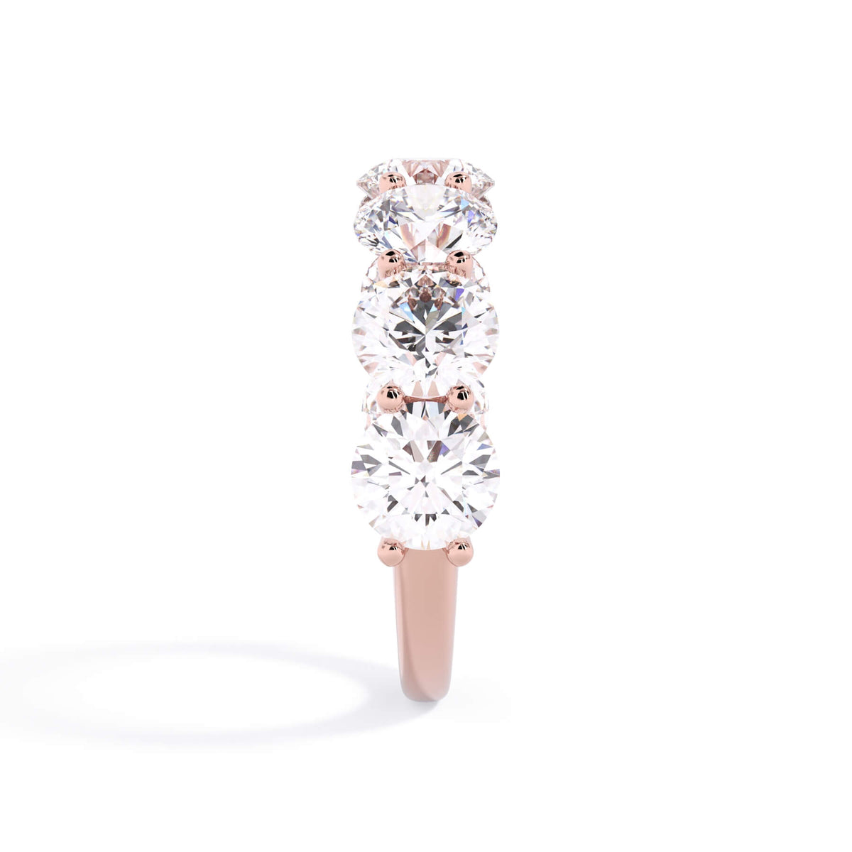 A picture of a seven stone diamond wedding ring with round diamonds that are U prong set in rose gold on a white background with a side profile view.