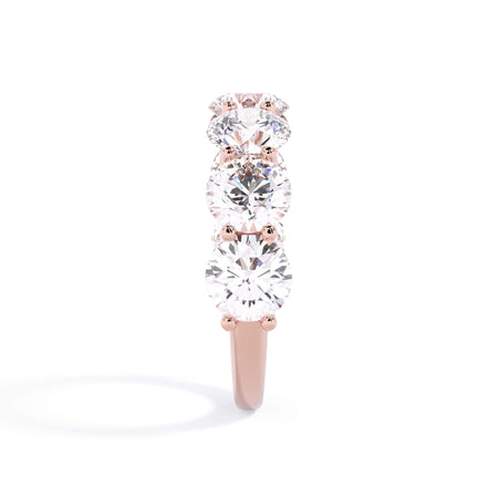 A picture of a seven stone diamond wedding ring with round diamonds that are U prong set in rose gold on a white background with a side profile view.