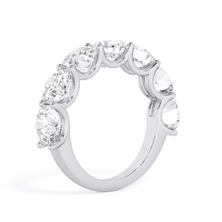 A picture of a seven stone diamond wedding ring with round diamonds that are U prong set in white gold or platinum on a white background with a slightly angled, through the finger view.