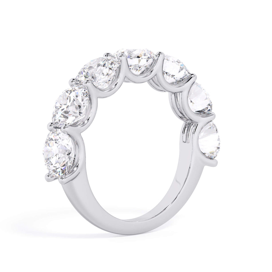 A picture of a seven stone diamond wedding ring with round diamonds that are U prong set in white gold or platinum on a white background with a slightly angled, through the finger view.