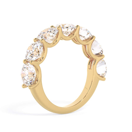 A picture of a seven stone diamond wedding ring with round diamonds that are U prong set in yellow gold on a white background with a slightly angled, through the finger view.
